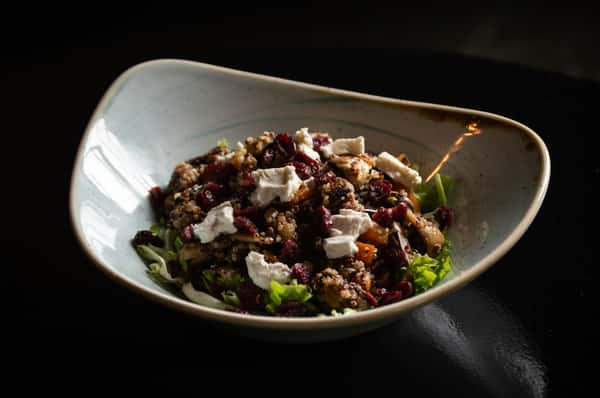 Quinoa salad with feta cheese, dried cranberries, and greens served in a ceramic bowl.
