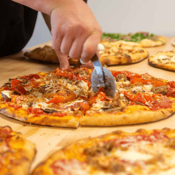 hand cutting a pizza with a pizza cutter