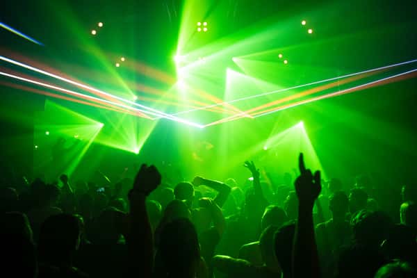 Crowd dancing under intense green laser lights at a nightclub concert, with arms raised and silhouettes outlined in the glow.