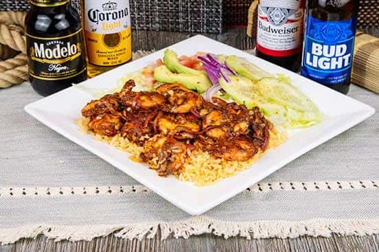 Spicy grilled shrimp over Mexican rice, paired with avocado, red onion, and cucumber salad, served on a white plate with assorted bottled beers including Modelo and Bud Light.