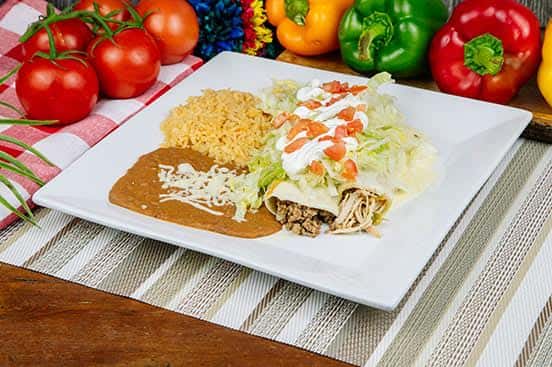 Mexican combo plate with a ground beef taco, chicken enchilada topped with lettuce, tomato, and sour cream, served with refried beans and seasoned Mexican rice.