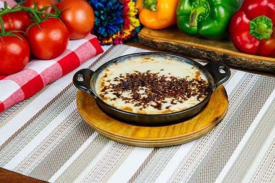 Mexican queso fundido in a cast iron skillet, featuring melted cheese topped with crumbled, seasoned chorizo, served on a wooden plate with a colorful pepper backdrop.
