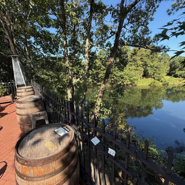 Outdoor patio with a wooden barrel table overlooking a tree-lined pond