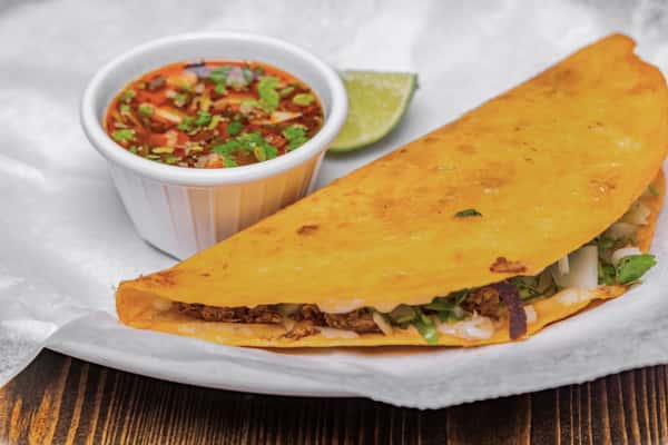 Crispy quesabirria taco filled with shredded beef, onions, and cilantro, served with a side of consommé and lime wedge.