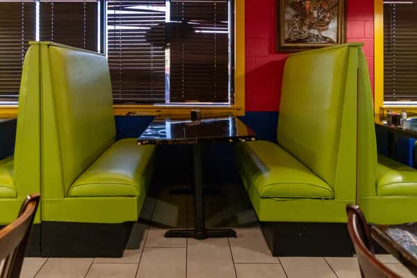Bright green vinyl booths with a glossy black table set against bold red and blue walls in a retro-style diner setting.