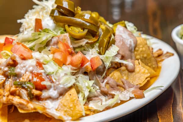 Loaded nachos topped with shredded lettuce, diced tomatoes, jalapeños, beans, melted cheese, and a dollop of sour cream.