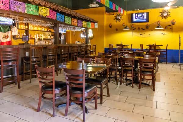 Colorful Mexican restaurant interior with papel picado, green booths, dark wood tables, and festive red, yellow, and blue walls.