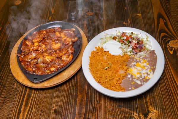 That's a sizzling shrimp fajita platter served with a classic Mexican combo plate — rice, refried beans topped with cheese, lettuce, pico de gallo, and a dollop of sour cream. A delicious and hearty meal with bold, smoky flavors!c