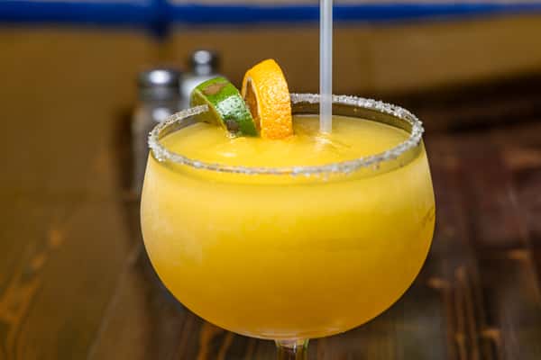 Frozen mango margarita in a salt-rimmed glass, garnished with lime and orange slices, served on a rustic wooden table.