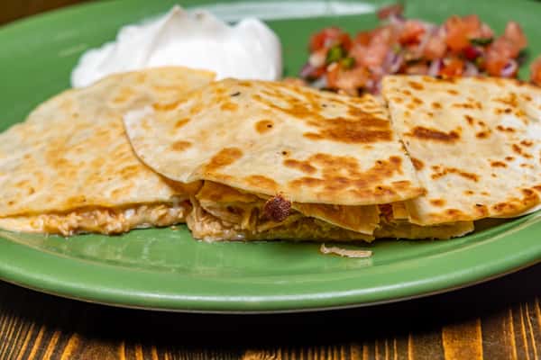 Golden chicken quesadillas with melted cheese, served with sour cream and fresh pico de gallo on a green plate.