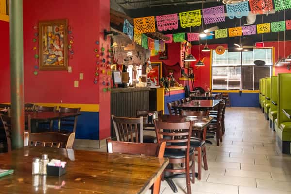 Colorful Mexican restaurant interior with papel picado, green booths, dark wood tables, and festive red, yellow, and blue walls.
