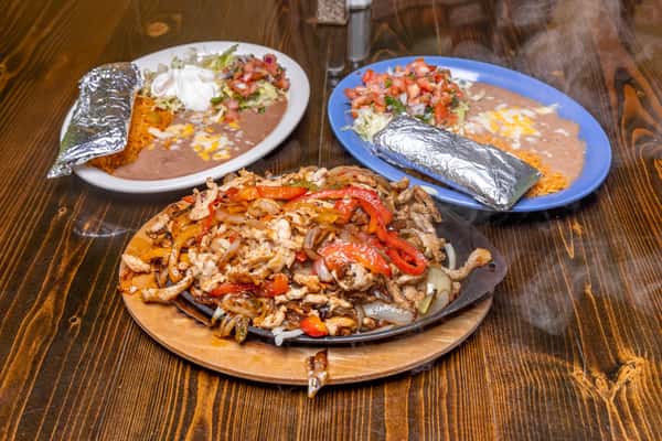 Steaming chicken fajitas with grilled peppers and onions, served with rice, beans, pico de gallo, and foil-wrapped tortillas.