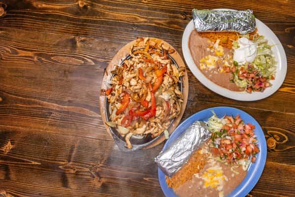 Sizzling chicken fajitas with grilled peppers and onions, served with foil-wrapped burritos, rice, beans, and fresh pico de gallo.