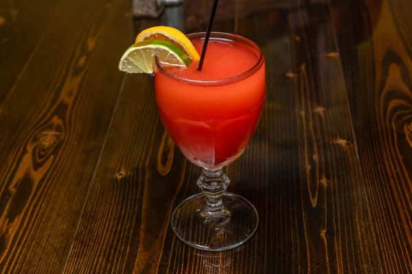 Frozen strawberry cocktail in a tall goblet glass, garnished with lime and orange slices, served on a wooden table.