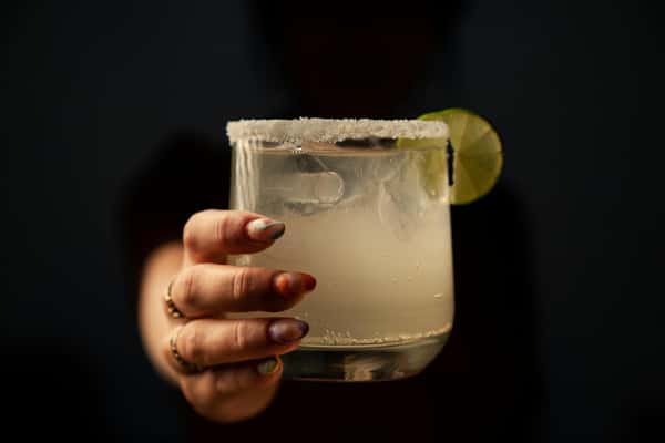 A margarita in a glass with a salted rim and a lime wedge, held by a hand.