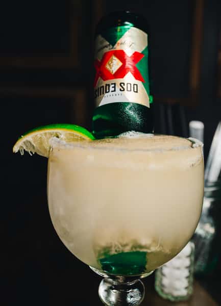 A margarita with a Dos Equis beer bottle placed upside down, garnished with a lime wedge, and served in a large glass.
