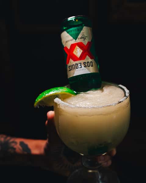 A margarita with a Dos Equis beer bottle placed upside down, garnished with a lime wedge, and served in a large glass.