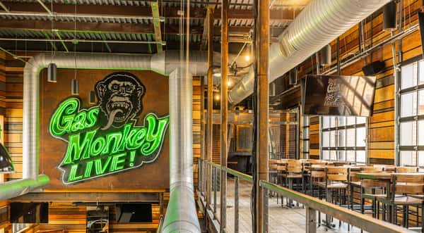 An interior view of Gas Monkey Live! with a neon "Gas Monkey Live!" sign, high tables, and a TV displaying the Gas Monkey Ice House logo.