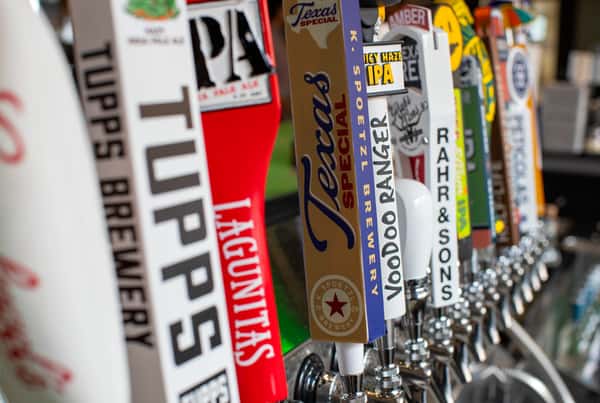 A close-up of several beer taps featuring various brewery logos, including Tupps, Lagunitas, Texas Special, Voodoo Ranger, and Rahr & Sons.