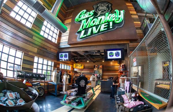 The interior of a Gas Monkey Live! venue, featuring a neon "Gas Monkey Live!" sign, merchandise displays, and a shop area with clothing and accessories.