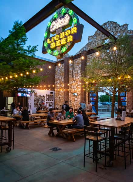 An outdoor seating area with string lights, tables, and people enjoying drinks, with a neon "Circle Liquor Beer" sign above the entrance.
