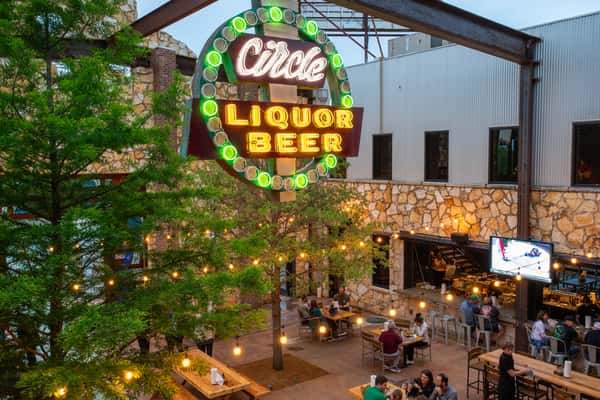 The outdoor seating area with string lights and a neon "Circle Liquor Beer" sign, showing people dining and a sports game on a nearby TV.