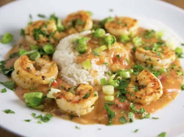 A scoop of white rice topped with shrimp, brown sauce, and scallions