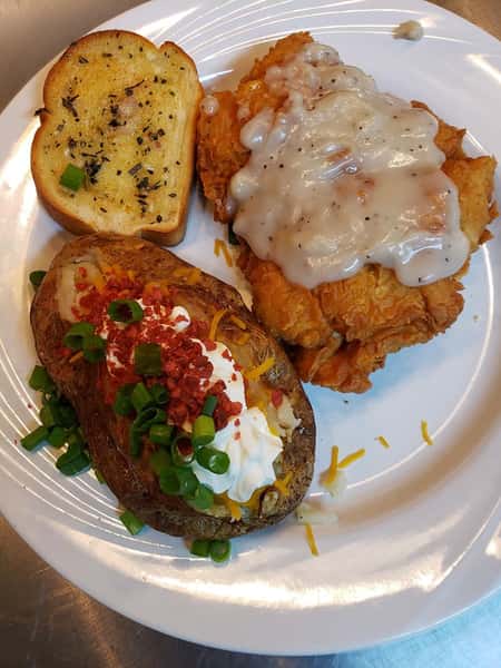 Chicken fried steak topped with gravy, with a side of garlic bread and a loaded baked potato