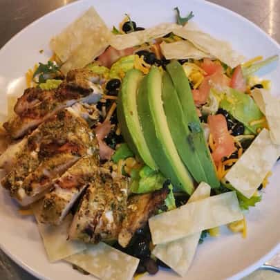 Chef salad topped with avocado, beans, tomato, cheese, chicken, and tortilla chips