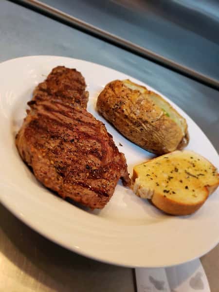Steak topped with butter, with a side of a loaded baked potato and garlic bread