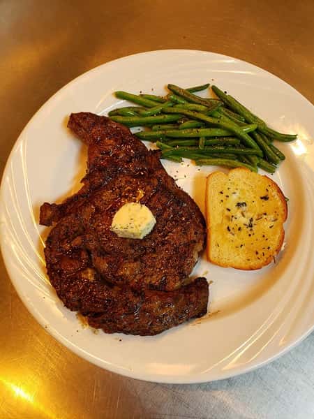 A steak with butter, garlic bread, and green beans