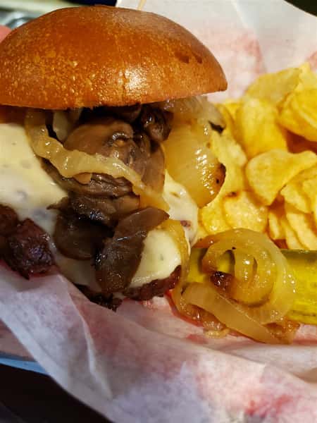 loaded steak sandwich with cheese, onions and a side of chips