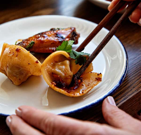 Hand using chopsticks to pick up a dumpling from a plate