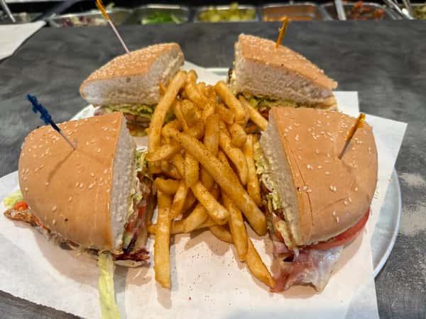 A large club sandwich cut into four pieces, served with seasoned French fries on a white tray at Texas Borders Bar & Grill.
