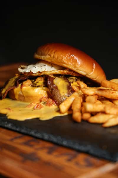 Cheeseburger topped with bacon, fried egg, and melted cheese, served with curly fries