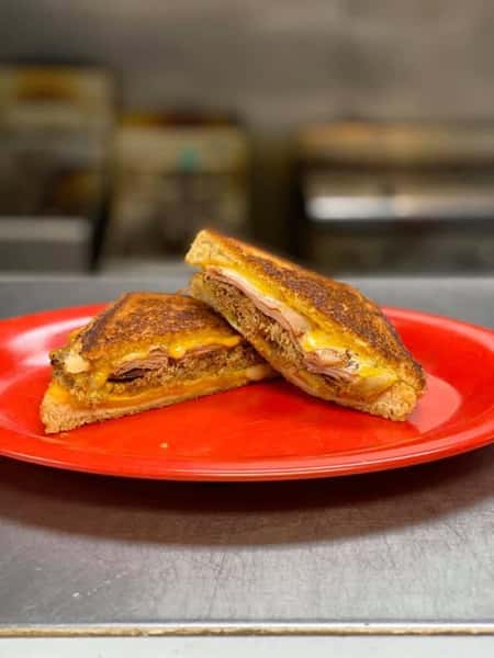 Grilled sandwich with pulled pork, ham, and melted cheddar cheese on toasted bread, served on a red plate.