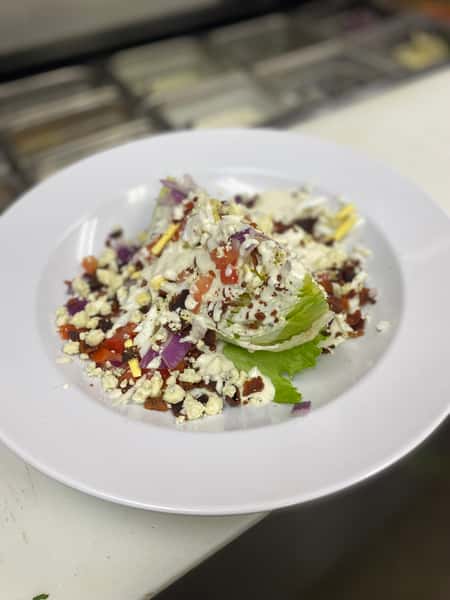 Fresh wedge salad topped with blue cheese crumbles, diced tomato, bacon bits, and creamy dressing.