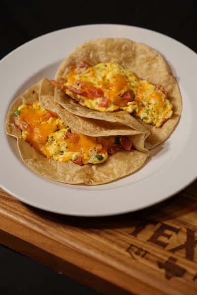 Two breakfast tacos filled with scrambled eggs, cheese, and diced vegetables, served on flour tortillas.