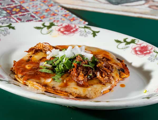 Cheese and shredded beef tostada topped with red sauce, melted cheese, onions, and cilantro