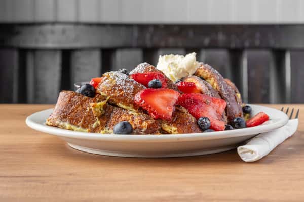 French toast topped with fresh strawberries, blueberries, powdered sugar, and whipped butter, classic brunch dish on a white plate