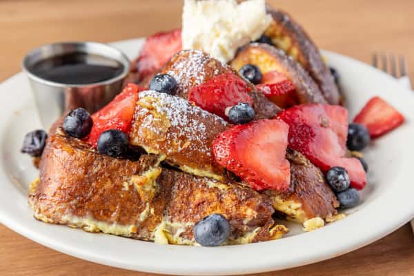 French toast with fresh strawberries, blueberries, powdered sugar, and butter served with syrup, classic brunch favorite