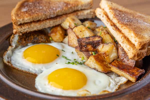 Two sunny-side-up eggs with crispy breakfast potatoes and toasted bread on a rustic plate, classic American diner breakfast dish