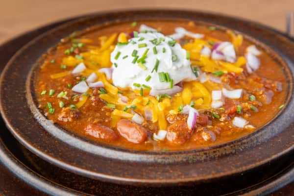Hearty bowl of chili topped with shredded cheese, sour cream, and diced onions, warm comfort food dish