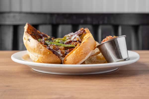 Juicy steak sandwich with grilled peppers and melted cheese on toasted bread, served with dipping sauce at an American diner