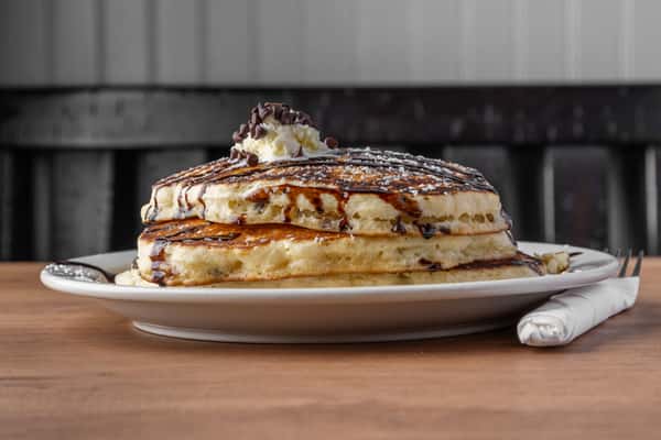 Fluffy pancakes with chocolate chips, powdered sugar, and chocolate drizzle topped with butter, classic diner breakfast