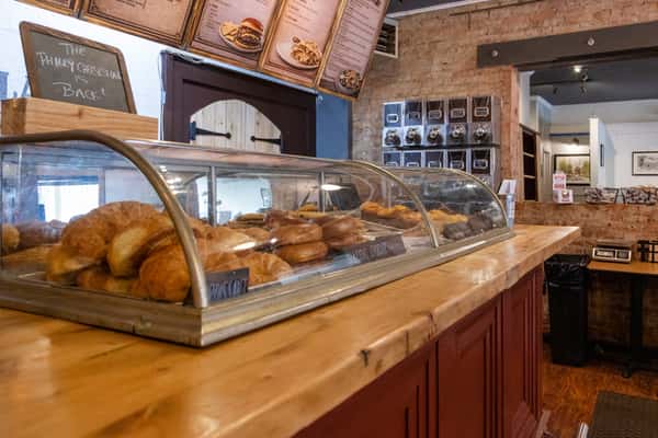 Bakery display case with fresh pastries and croissants on a wooden counter inside a cozy café