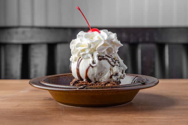 Decadent dessert with whipped cream, chocolate drizzle, and cherry on top served in a rustic diner setting