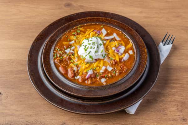 Hearty bowl of chili topped with shredded cheese, sour cream, and diced onions, classic comfort food dish