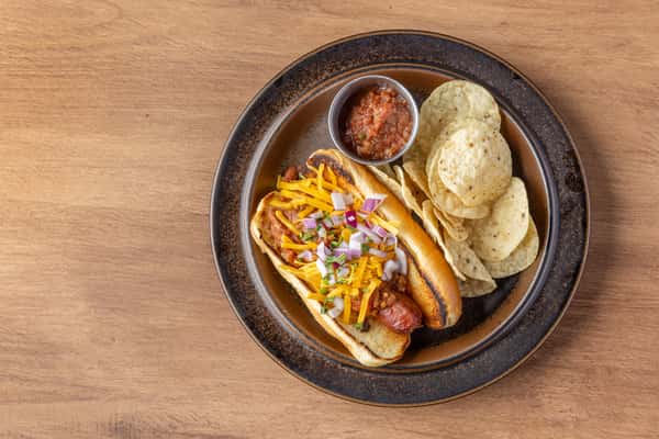 Chili cheese dog topped with shredded cheddar and diced onions, served with tortilla chips and salsa
