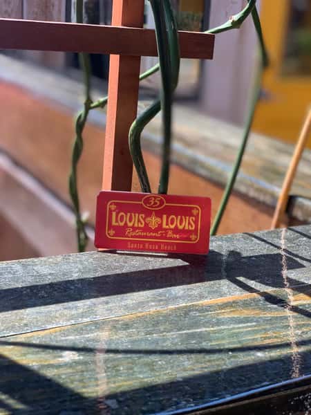 A "LOUIS LOUIS" restaurant table number sign featuring a red background with yellow text and a fleur-de-lis logo. The sign shows "35" and "Santa Rosa Beach."